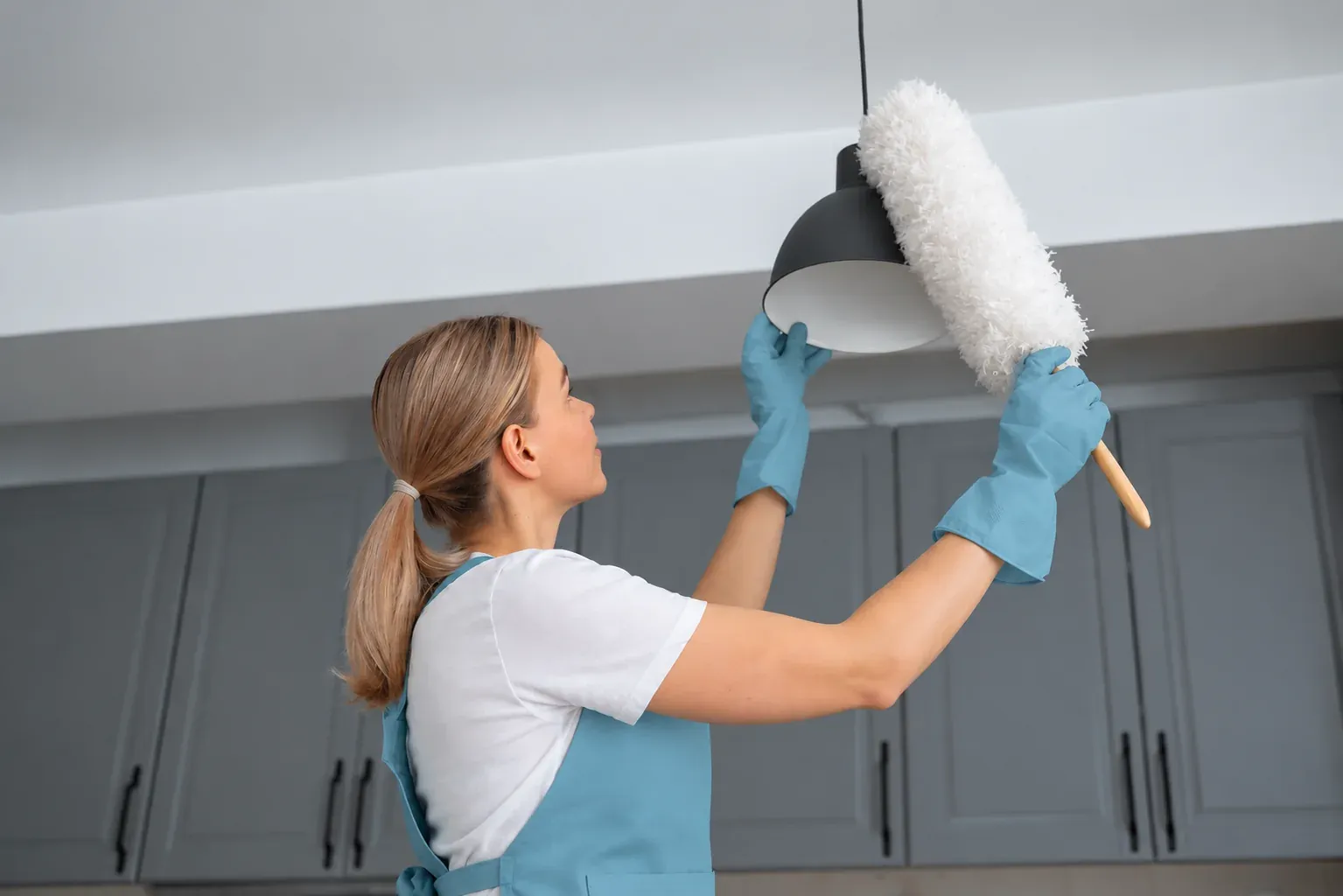 Cleaner dusting a ceiling light